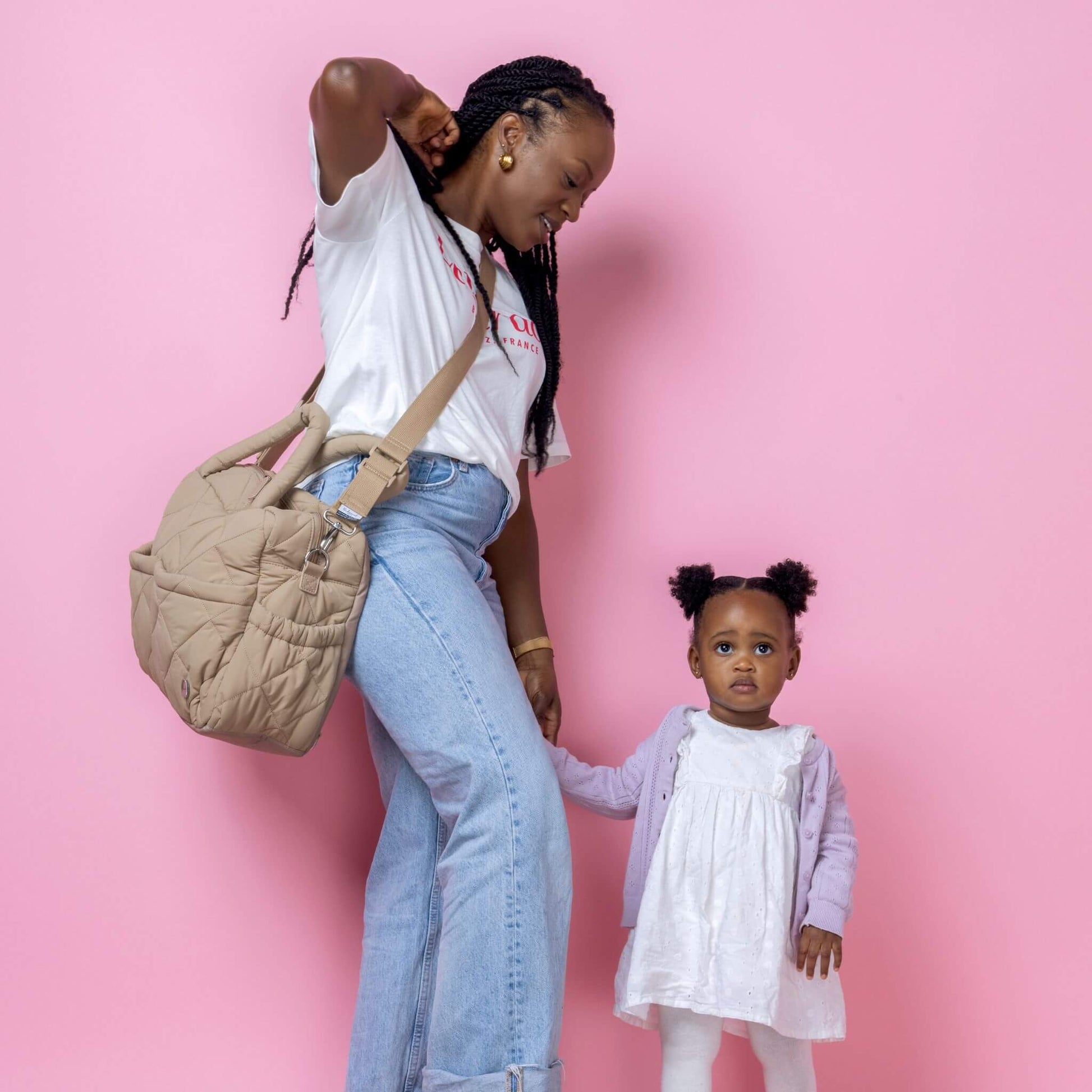 Babymel Willow Convertible Changing Bag in oatmeal, worn crossbody by a mother holding her toddler’s hand, showcasing its stylish and practical design.