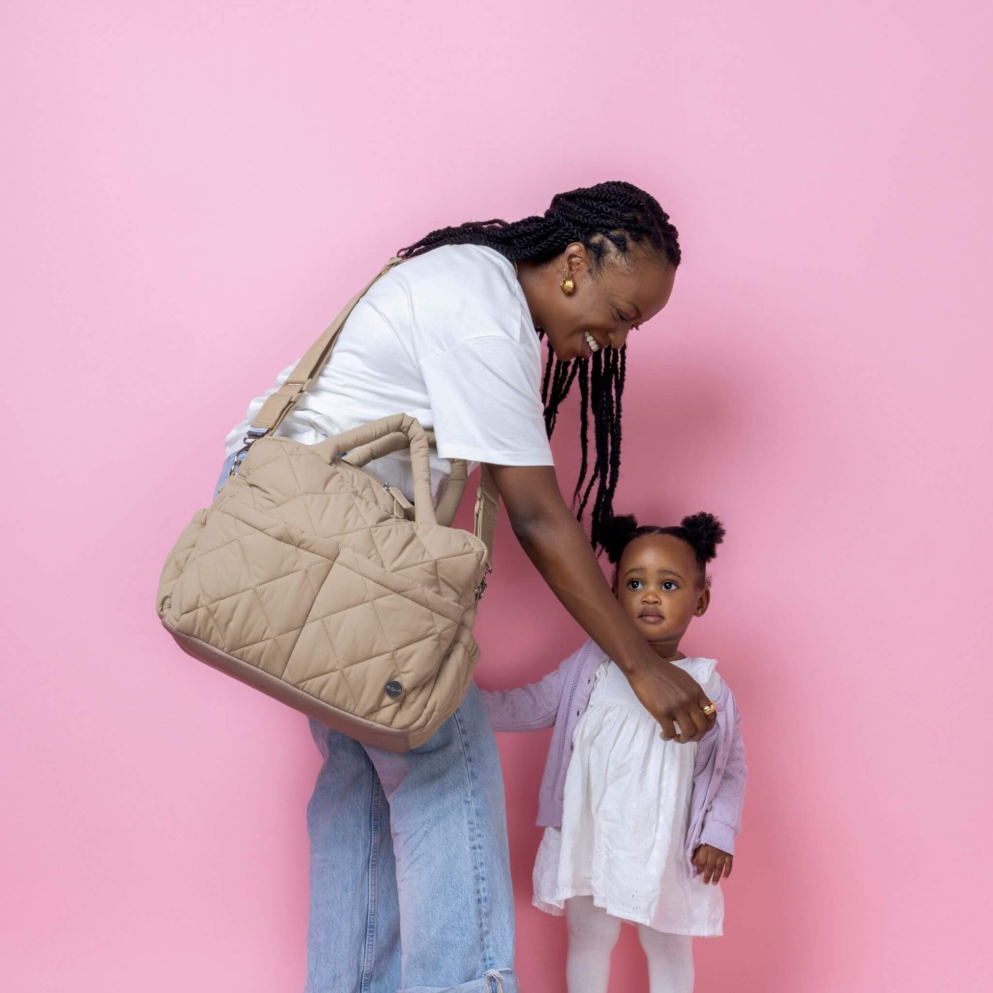 Babymel Willow Convertible Changing Bag in oatmeal, worn crossbody by a mother interacting with her toddler, highlighting its roomy and stylish design.