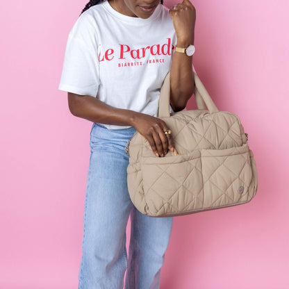 Babymel Willow Convertible Changing Bag in oatmeal, carried by a woman, highlighting its quilted texture, front pockets, and stylish versatility.