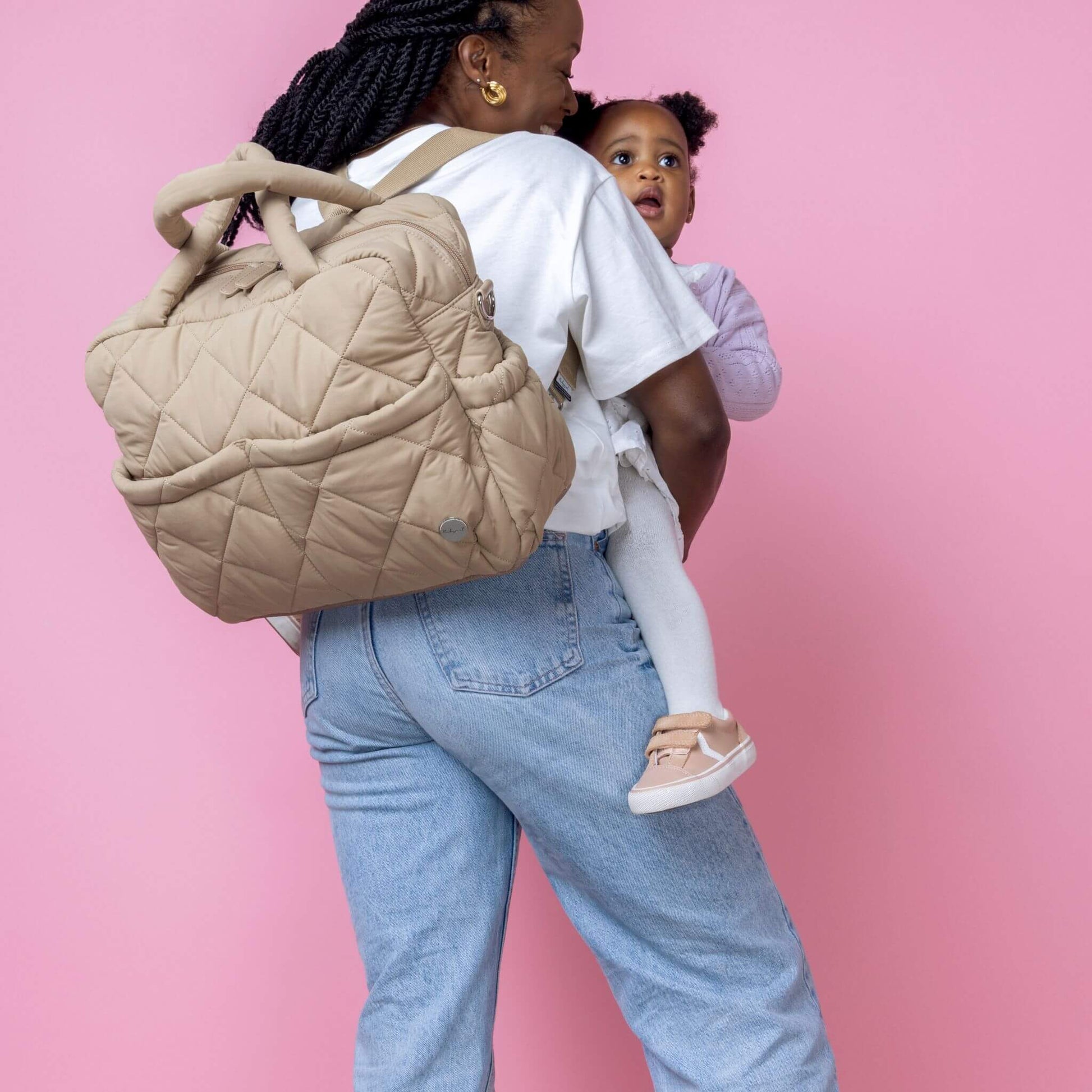 Babymel Willow Convertible Changing Bag in oatmeal, worn as a backpack by a mother carrying her baby, showcasing its hands-free practicality.