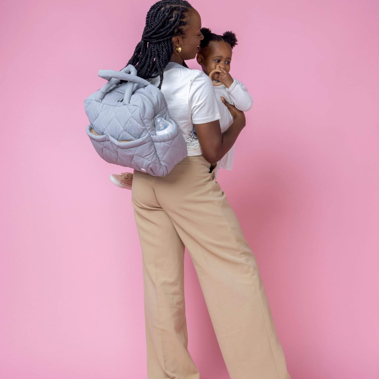 Babymel Willow Convertible Changing Bag in duck egg grey, worn as a backpack by a mother holding her baby, showcasing hands-free convenience.