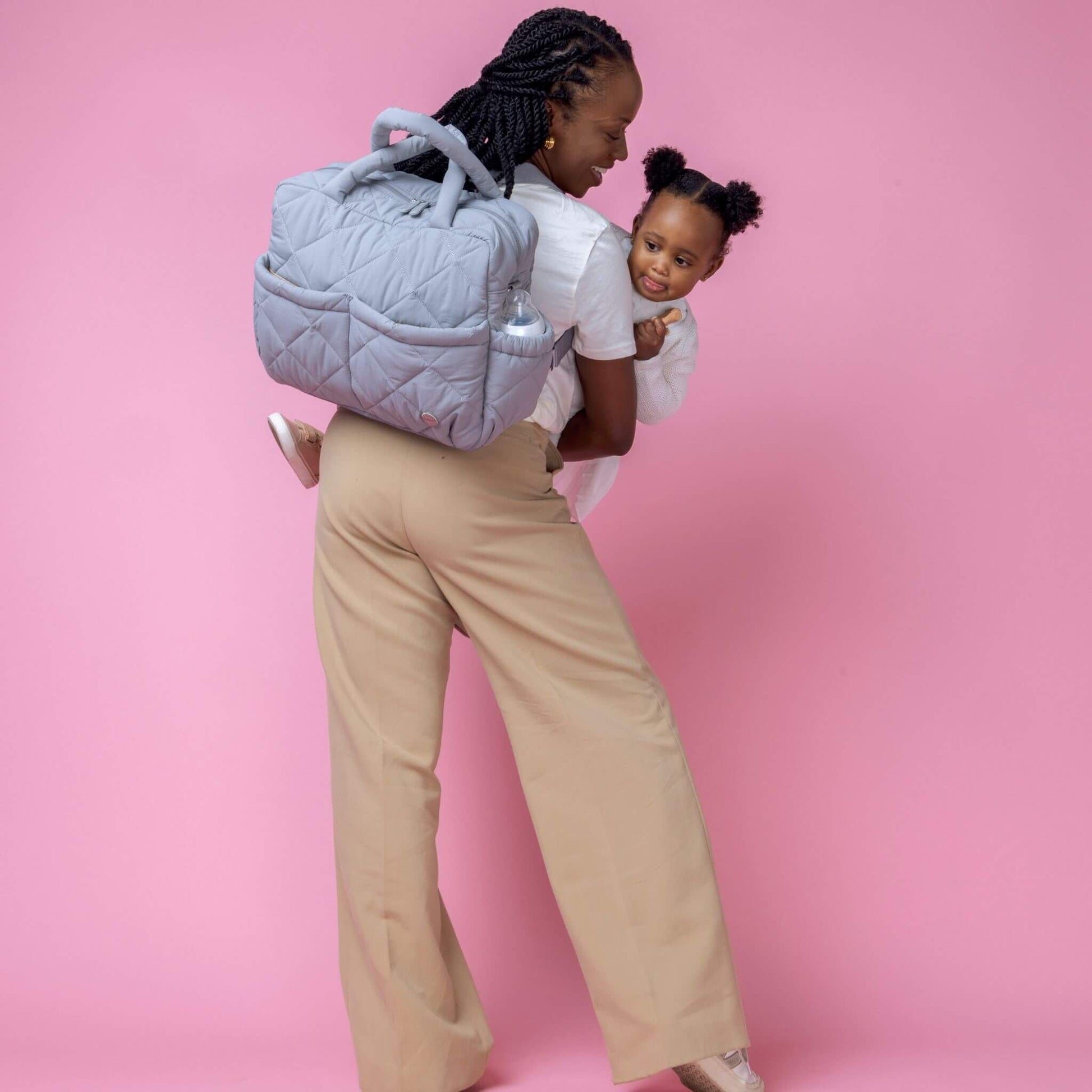 Babymel Willow Convertible Changing Bag in duck egg grey, worn as a backpack by a mother carrying her toddler, highlighting its hands-free versatility.