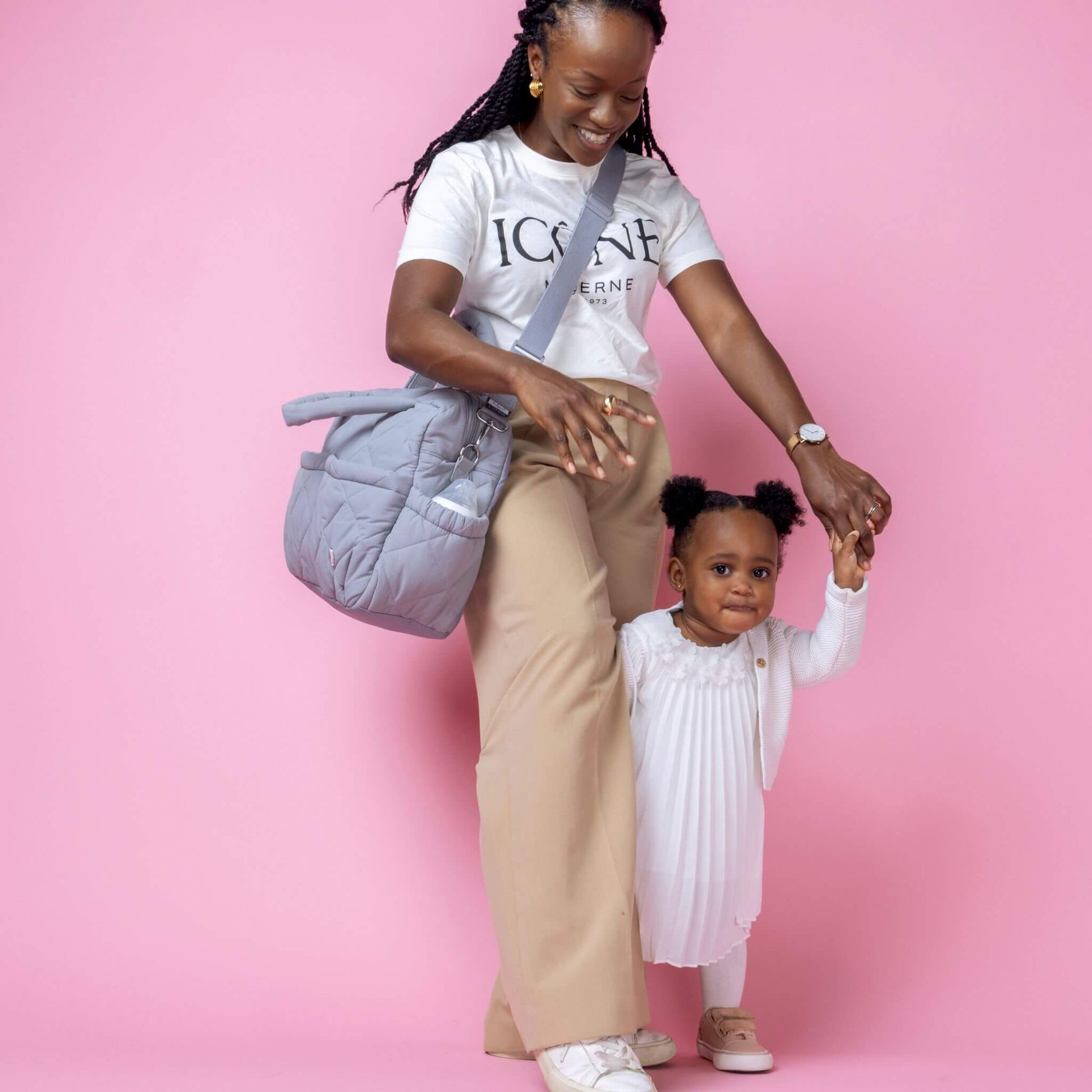 Babymel Willow Convertible Changing Bag in duck egg grey, worn crossbody by a smiling mother holding her toddler’s hand, showcasing its versatility.