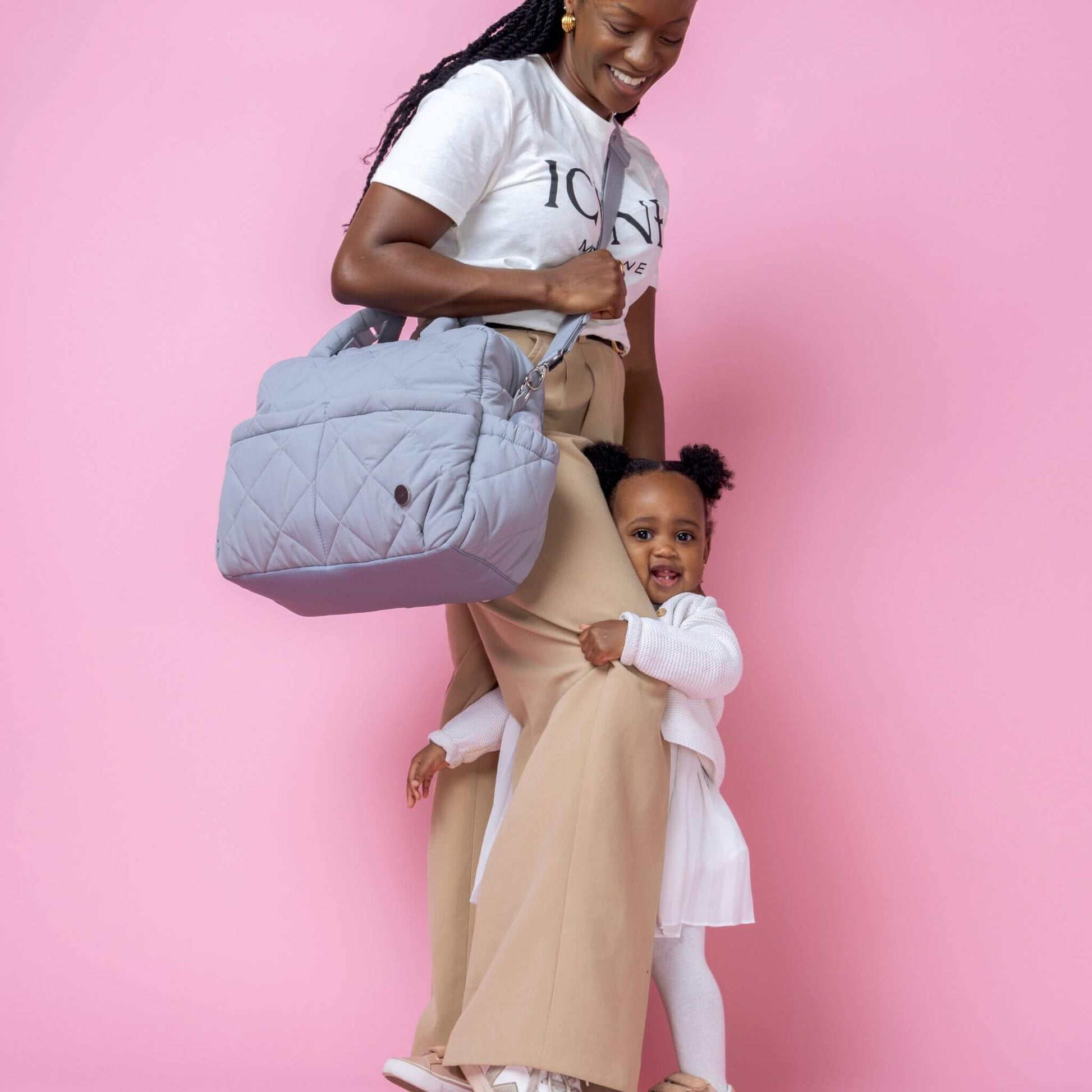 Babymel Willow Convertible Changing Bag in duck egg grey, worn crossbody by a smiling mother, with her toddler hugging her leg, showing everyday practicality.