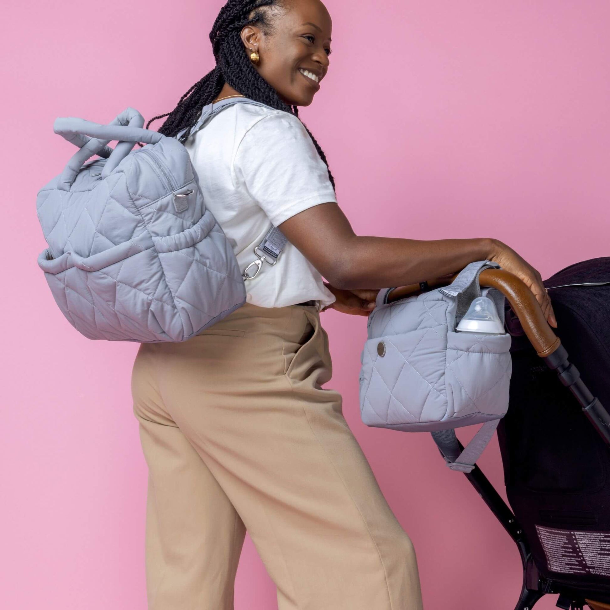 Babymel Willow Convertible Changing Bag in duck egg grey, worn as a backpack by a smiling mother, with a matching stroller bag attached to the pram.