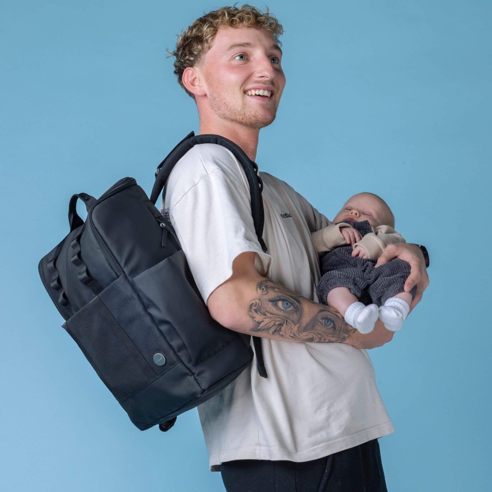 Parent wearing the Babymel Finn Changing Backpack in Black while holding a baby, highlighting its comfortable design and practicality for hands-free parenting.