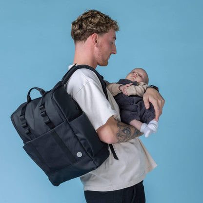 Side view of a parent wearing the Babymel Finn Changing Backpack in Black while cradling a baby, highlighting its ergonomic design and hands-free convenience for everyday parenting.