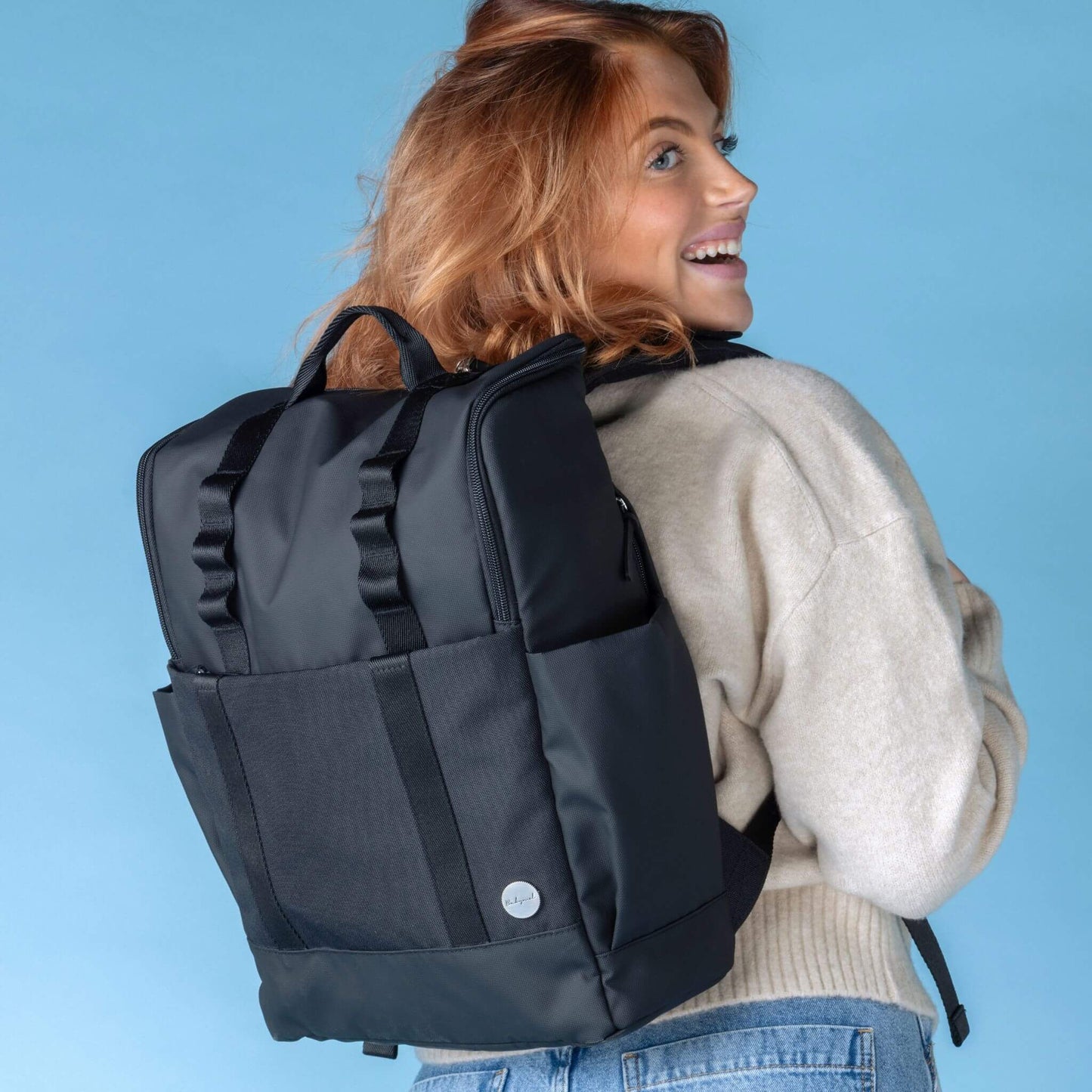 Smiling parent wearing the Babymel Finn Changing Backpack in Black, showcasing its comfortable fit and modern, practical design for everyday use.