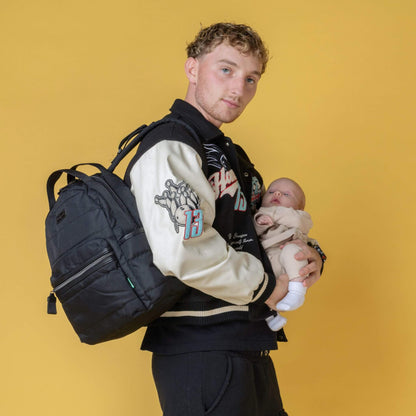 Father holding a baby while wearing the Babymel Lola Eco Backpack in Black, showcasing its practicality and hands-free convenience.