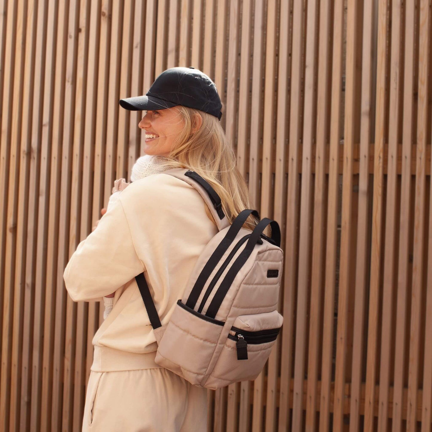 Mother smiling while carrying the Babymel Lola Eco Backpack in Fawn, highlighting its comfortable fit and stylish design for everyday use.