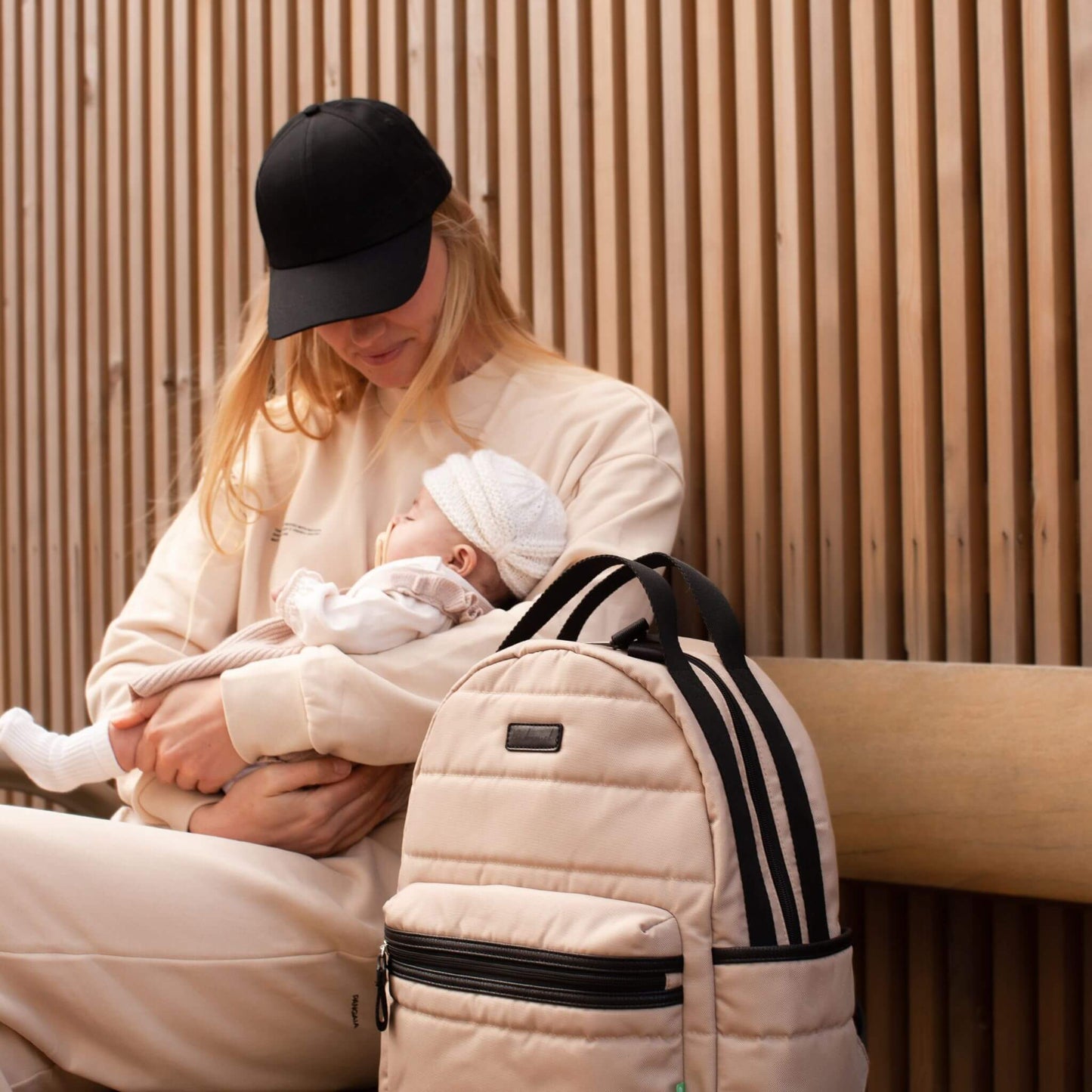 Mother seated with her baby and the Babymel Lola Eco Backpack in Fawn, highlighting its stylish and practical design for parenting on the go.