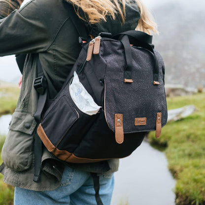 Person wearing the black Babymel Robyn Eco Convertible Backpack with tan details outdoors, showing its water-resistant design and easy-wipes pocket.