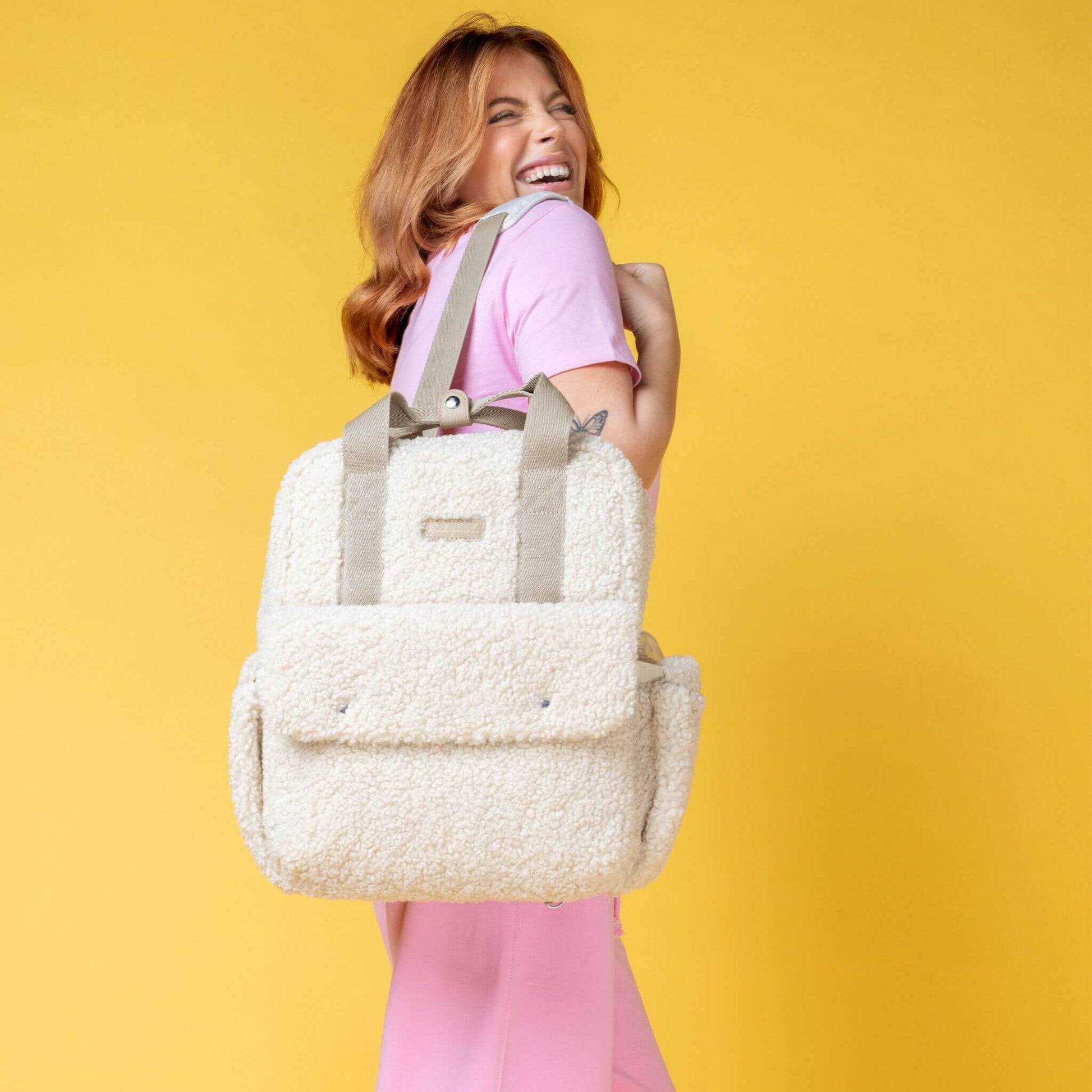 Smiling woman wearing the cream Babymel Teddy Convertible Backpack with soft borg fleece, styled as a shoulder bag, highlighting its cosy and stylish design.