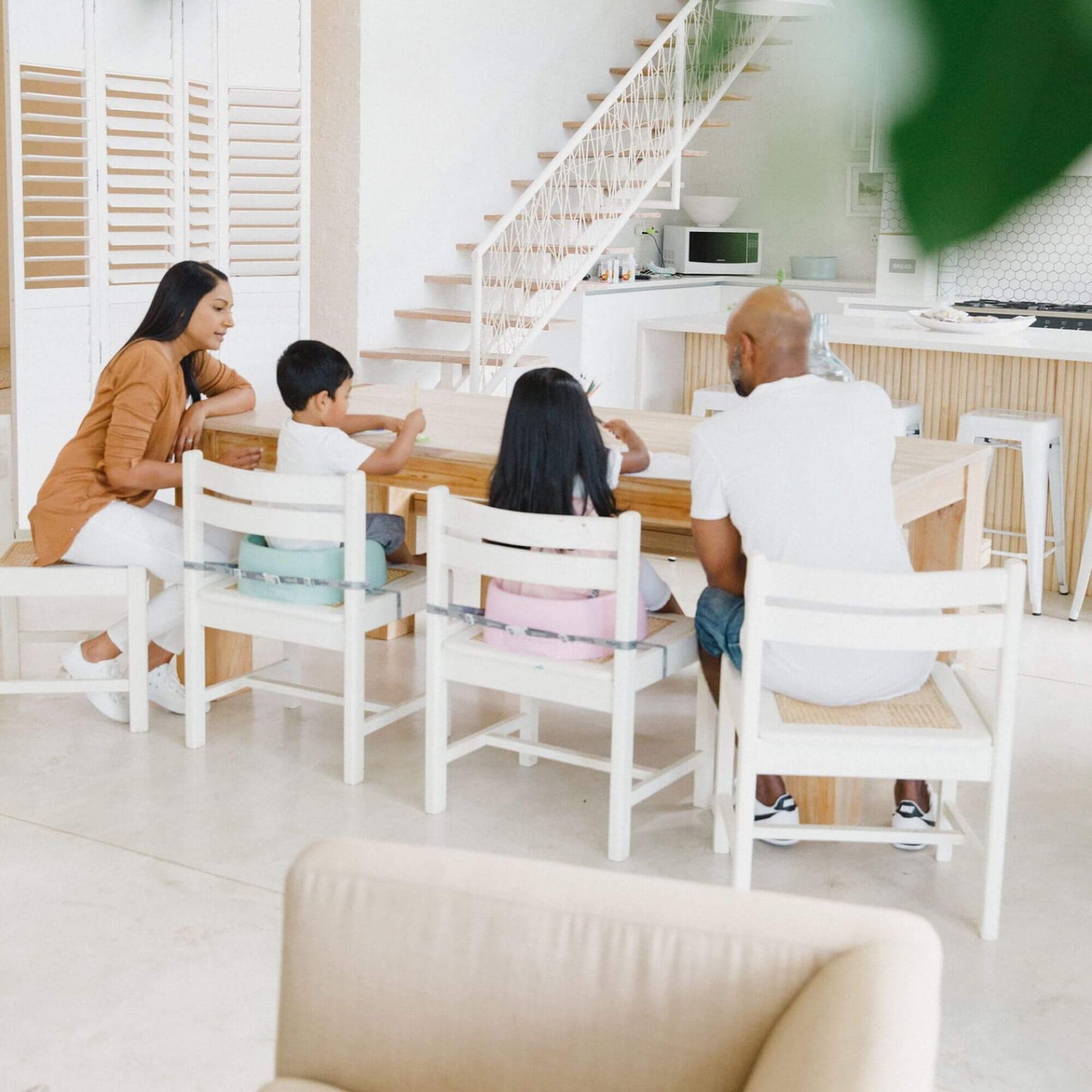 Family seated around a dining table, with two children in Bumbo booster seats securely strapped to their chairs.