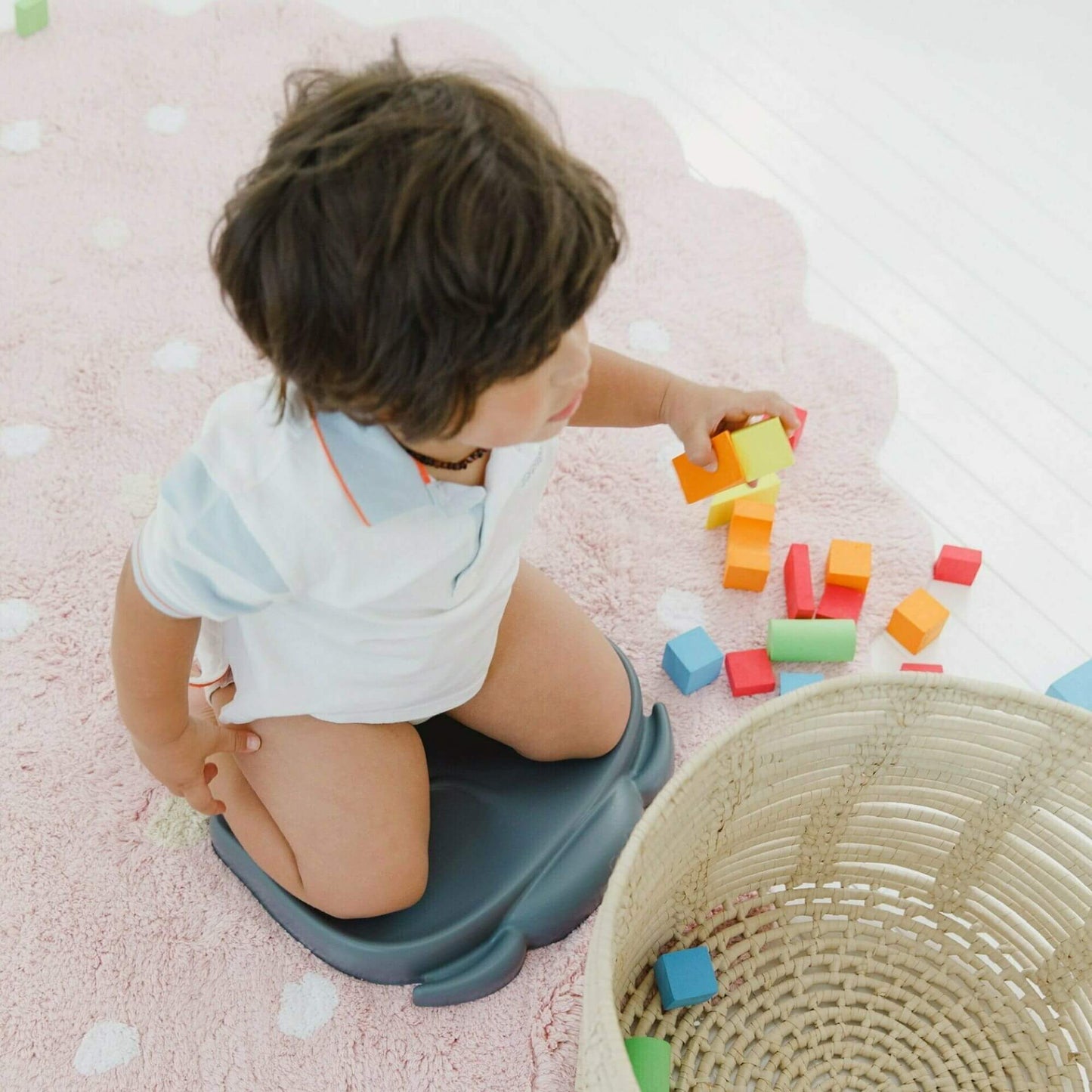 Toddler kneeling on a slate grey Bumbo Elipad, playing with colourful blocks on a soft pink rug for comfortable support during playtime.