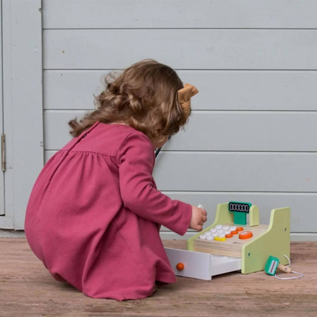 Child engaging with the Classic World Cash Register, using wooden coins, banknotes, and a scanner for imaginative role-play and learning.