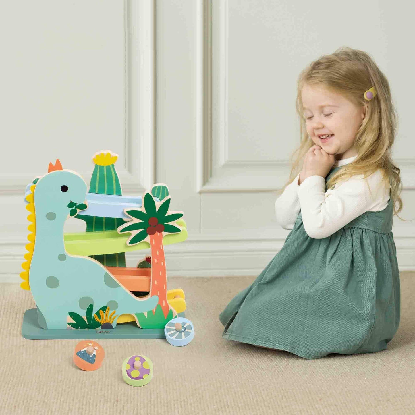 Smiling child playing with the Classic World Dinosaur Slide, featuring a fun dinosaur design, colourful tracks, and rolling wooden wheels.