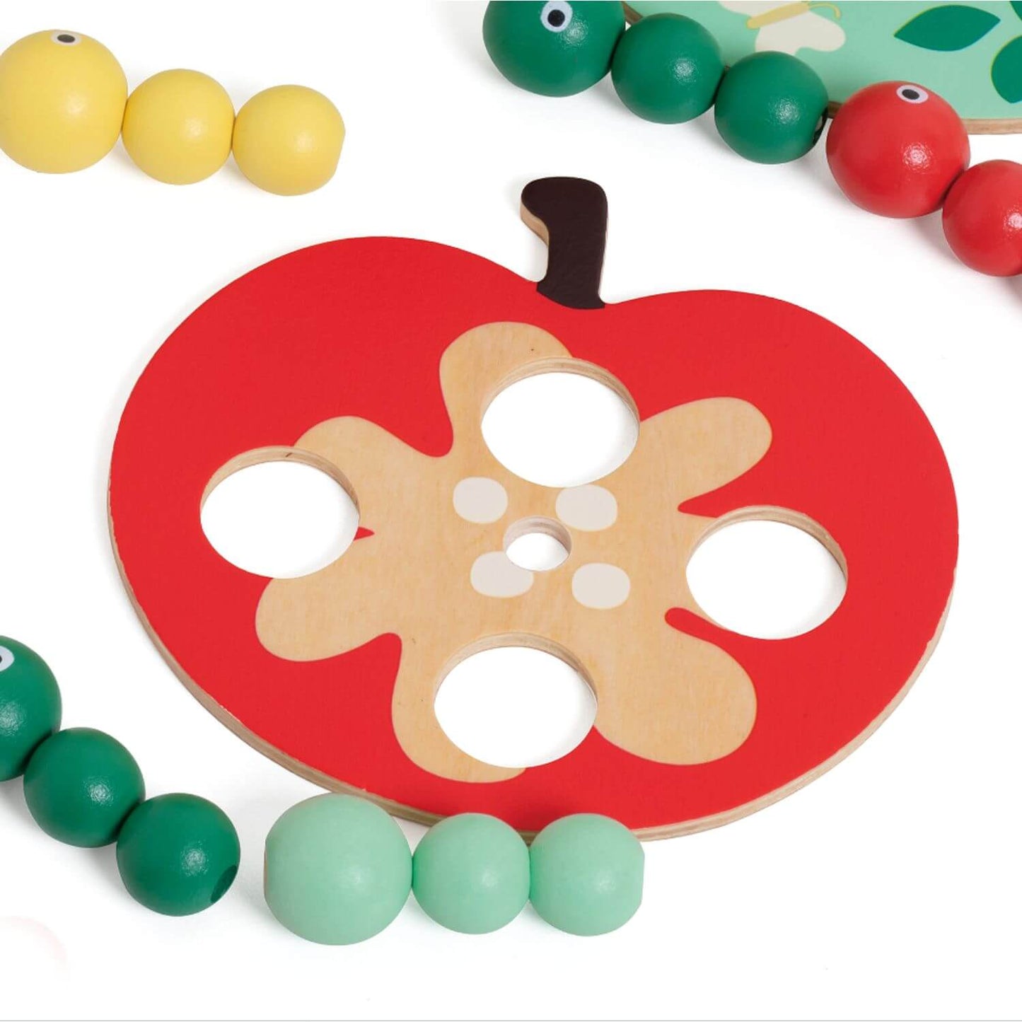 A close-up of the Classic World Doctor Woodpecker toy’s red wooden apple piece with cut-out holes, surrounded by colourful magnetic worms.