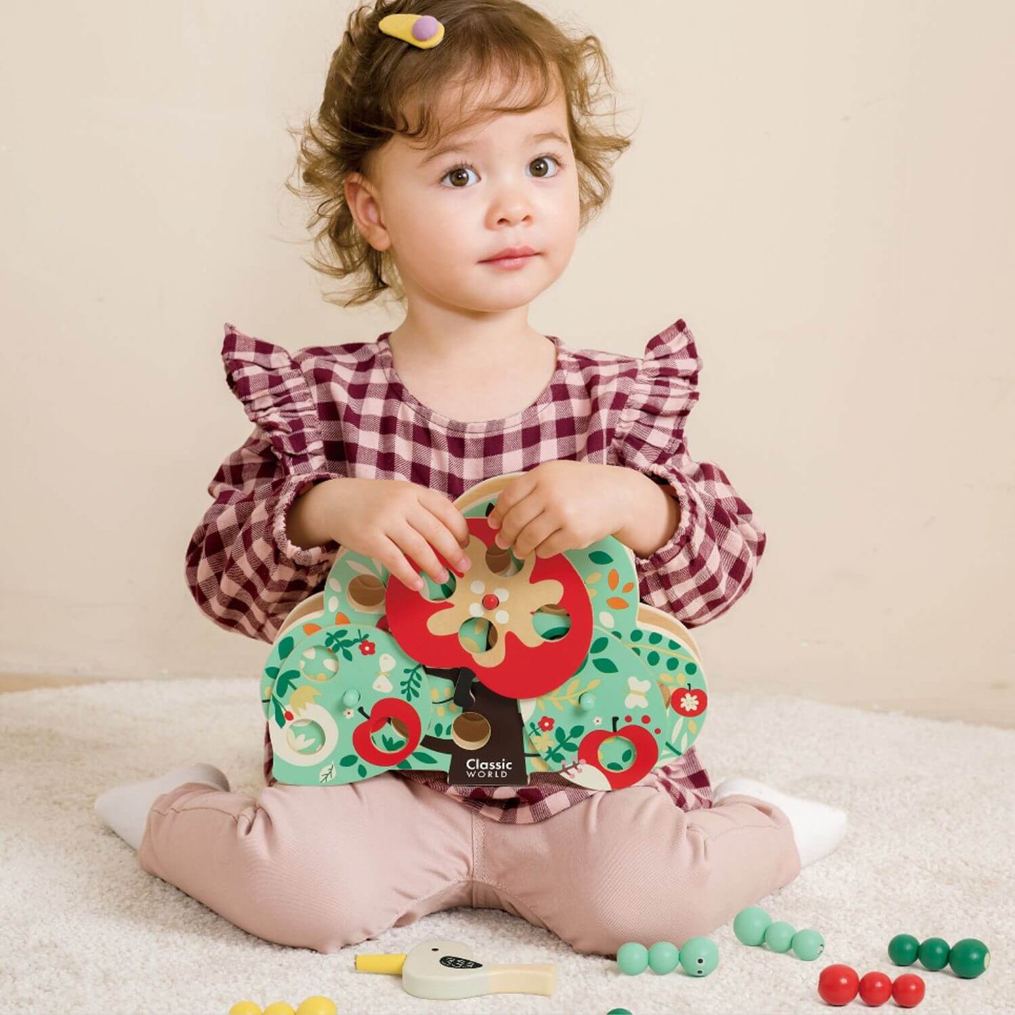 A young child playing with the Classic World Doctor Woodpecker toy, holding the colourful wooden apple tree surrounded by magnetic worms.