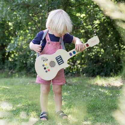 Young child exploring music outdoors with the Classic World Electric Glowing Wooden Guitar, highlighting its playful design and colourful keys.