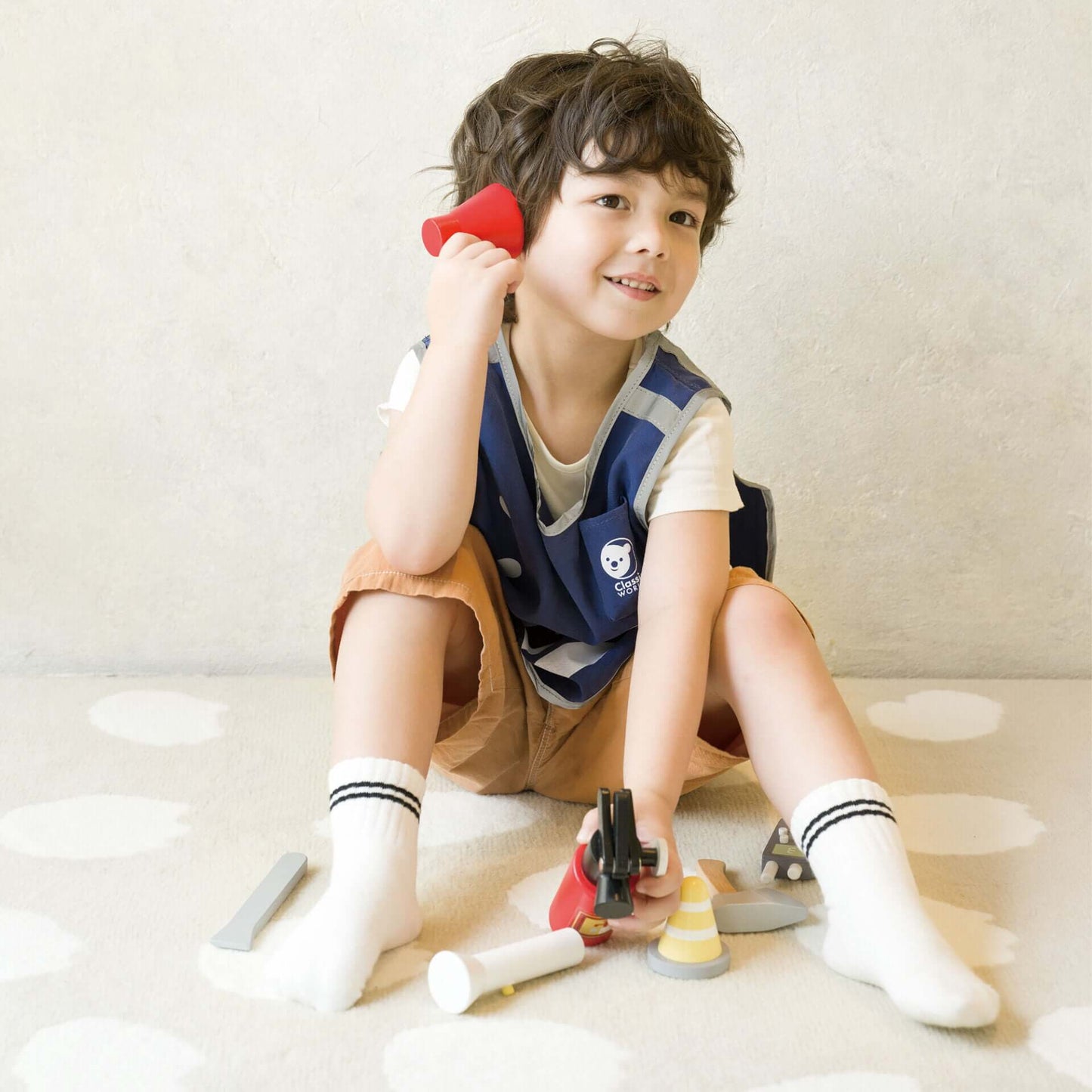 Child dressed in the Classic World Firefighting vest, holding a red megaphone and surrounded by rescue tools, ready for role-play fun