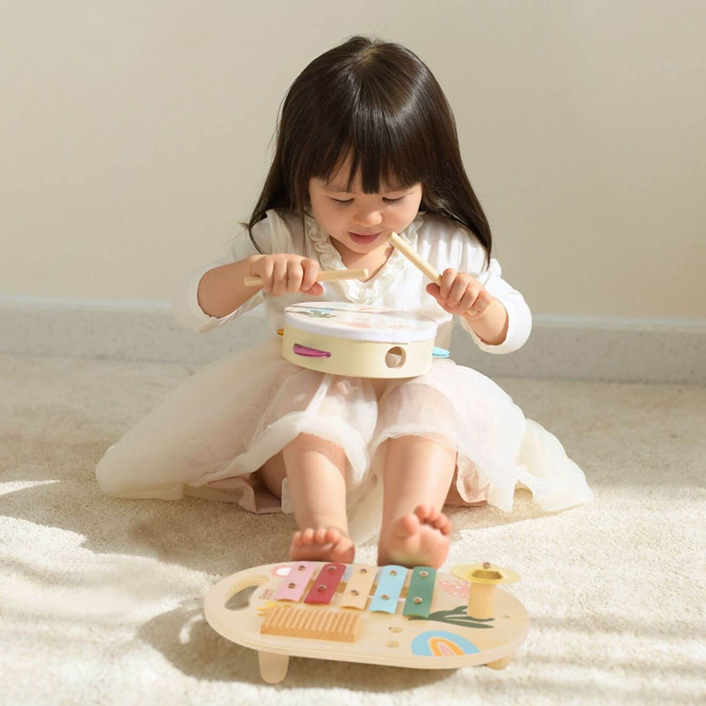 A young girl joyfully playing the tambourine from the Classic World Iris Music Set, with the xylophone nearby, creating musical fun.