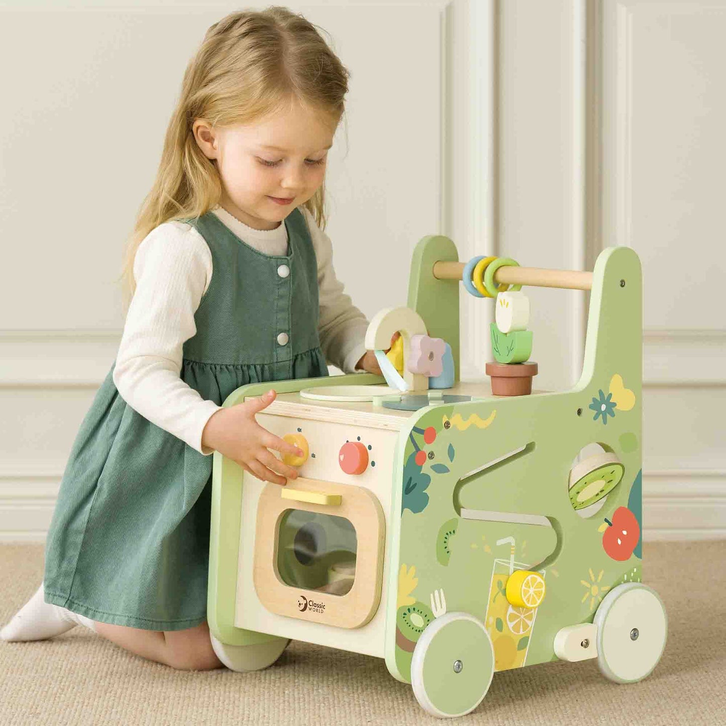 Child playing with the Classic World Kitchen Walker, featuring a wooden play kitchen with interactive knobs, utensils, and colourful designs.