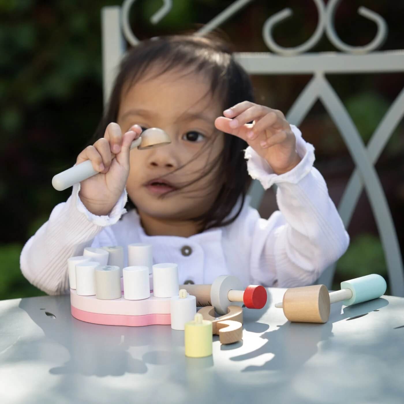 A child sits outdoors, deeply engaged with the Classic World Little Dentist Set, holding wooden dental tools while examining a piece.