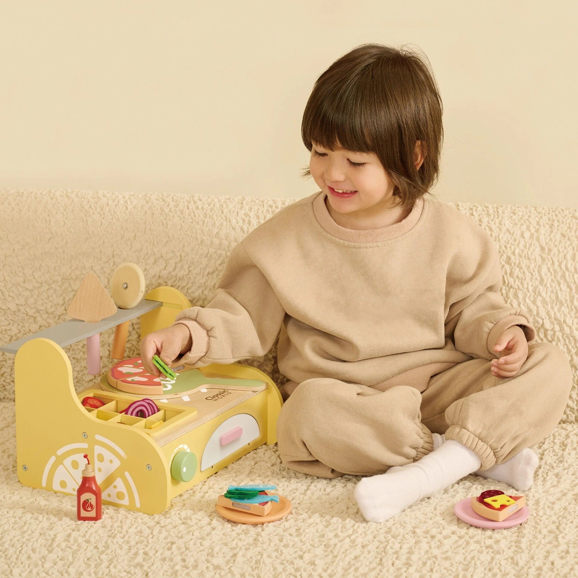 Smiling child playing with the Classic World Pizza Oven, assembling wooden pizza slices with colourful toppings for imaginative kitchen fun.