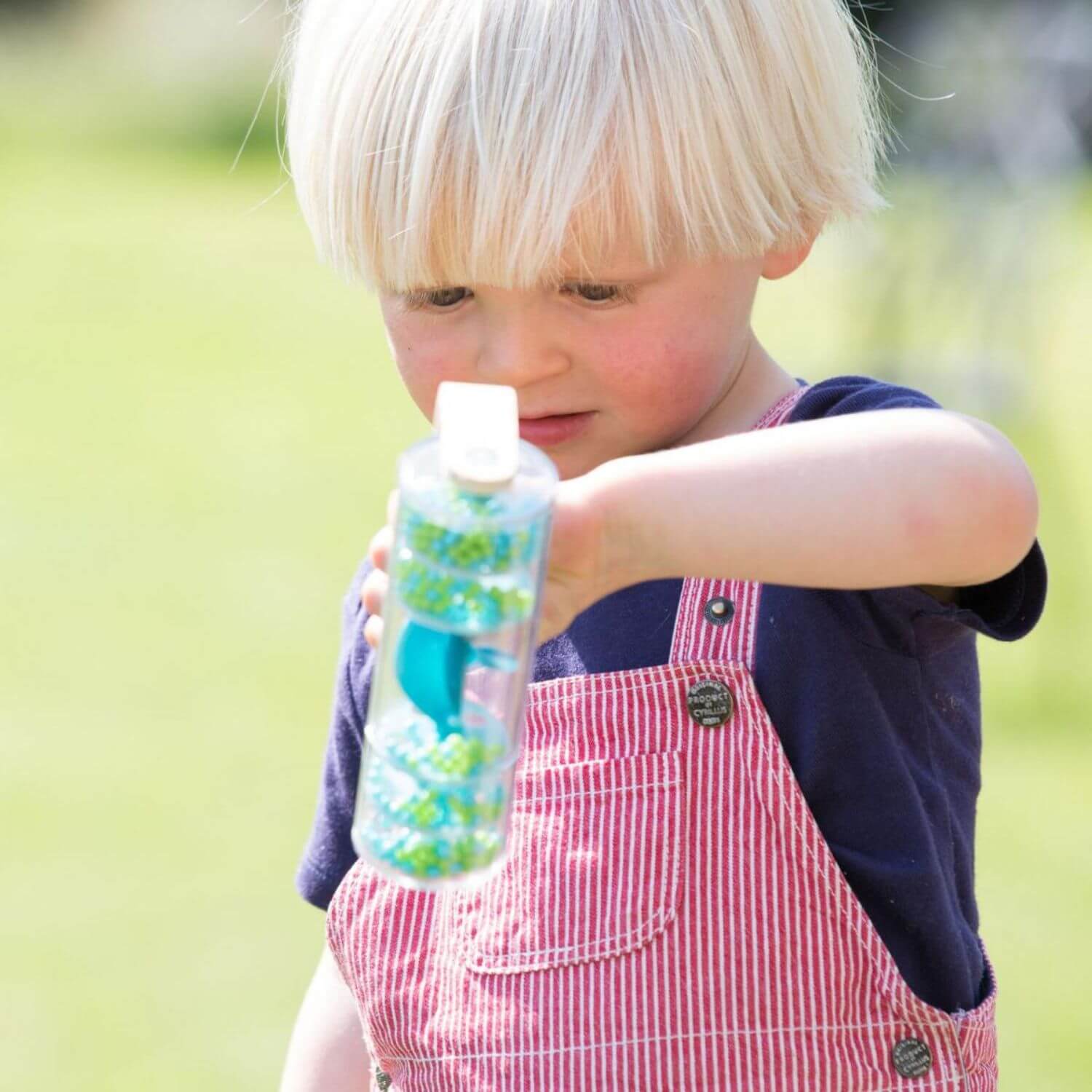 A child holding and observing the Classic World Rainmaker toy outdoors, fascinated by the colourful beads cascading inside.