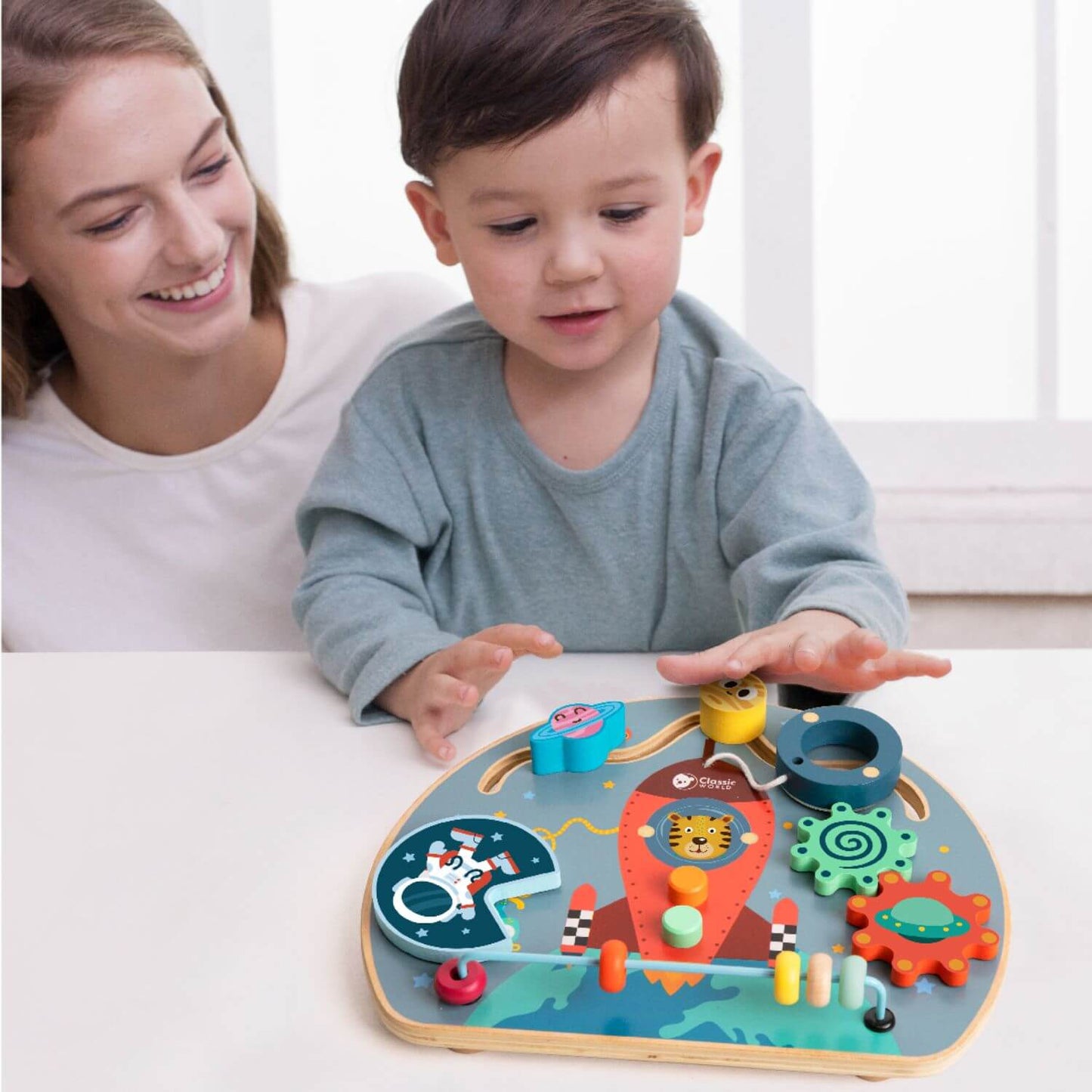 Child playing with the Classic World Rocket Busy Board while a smiling mother watches on.