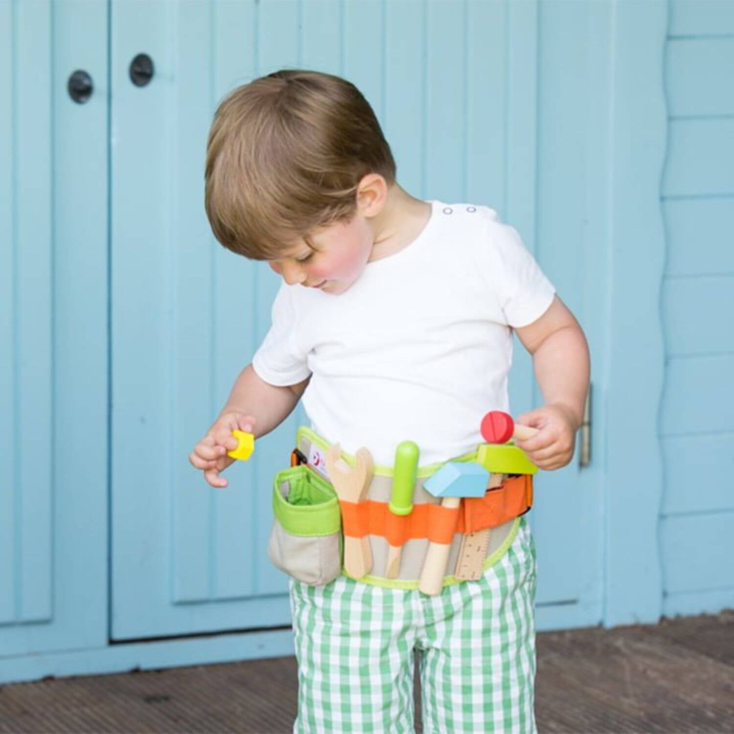 A young boy wearing the Classic World Tool Belt, exploring the wooden tools and accessories, showcasing its fun and educational design for imaginative play.