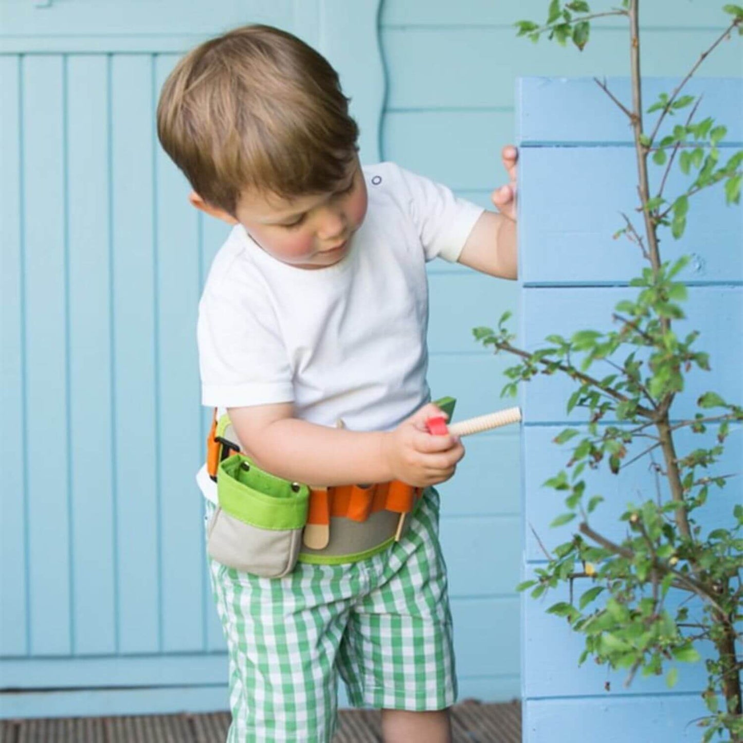 A young boy wearing the Classic World Tool Belt, using the wooden screwdriver for pretend play, showcasing its interactive and portable design.