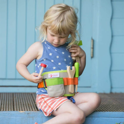 A young girl examining the tools in the Classic World Tool Belt, featuring a colourful adjustable design with wooden hammer, wrench, and screwdriver.