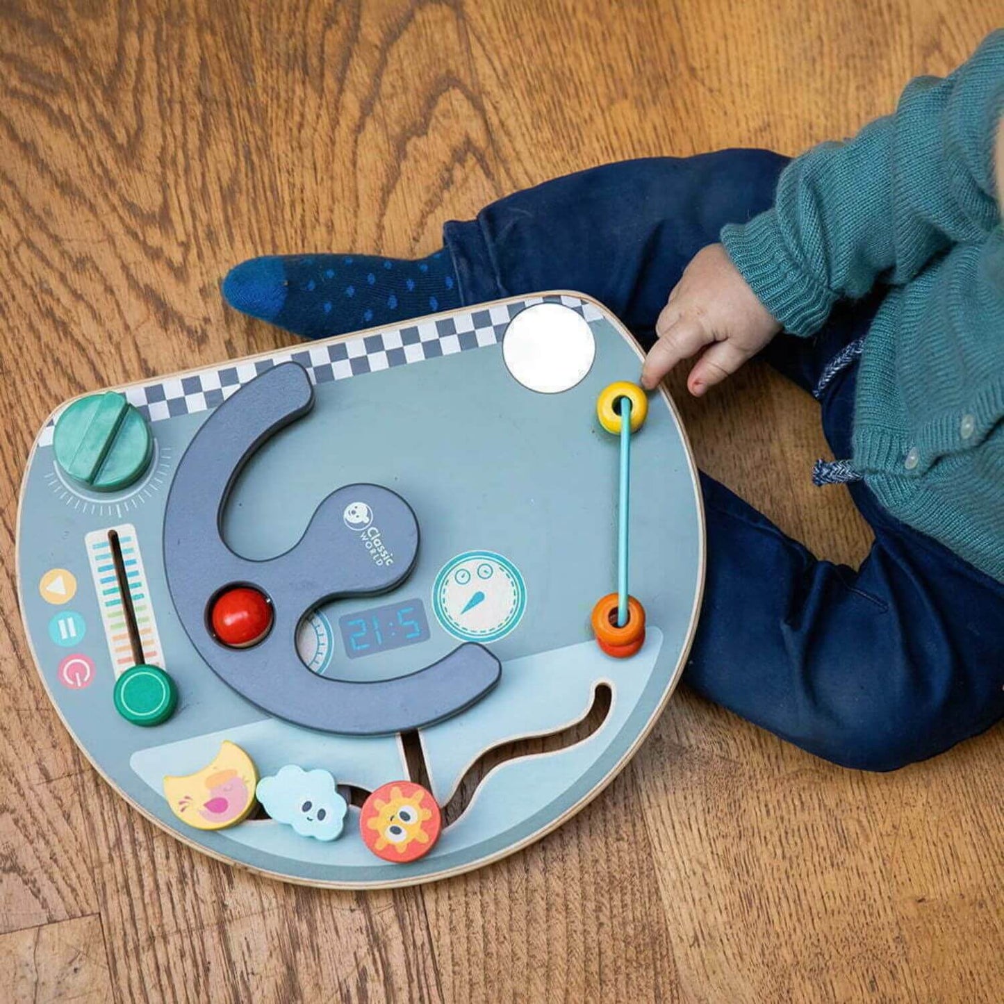 Toddler engaging with the Classic World Travel Busy Board, focusing on its interactive features like the bead slider and maze elements.