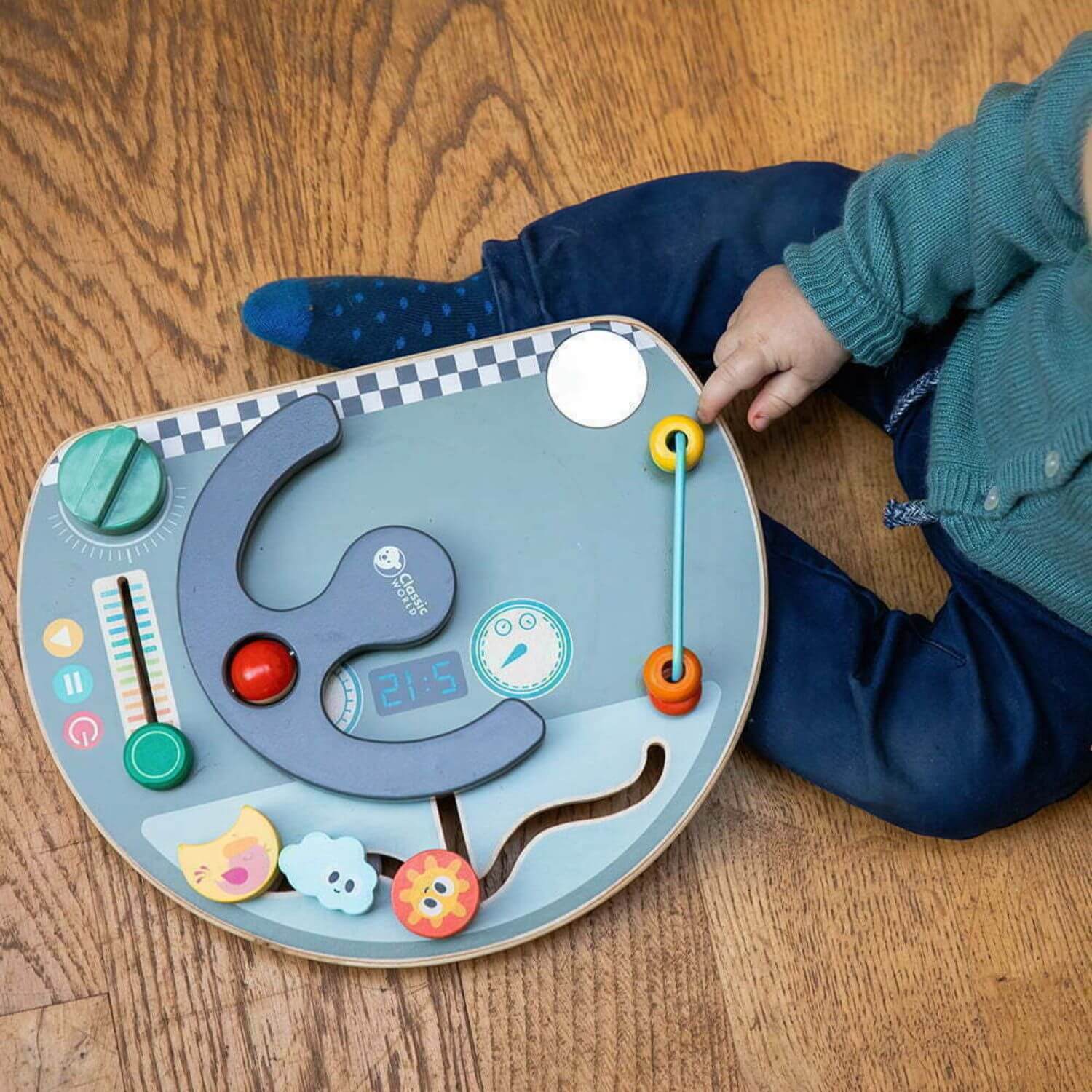 Toddler engaging with the Classic World Travel Busy Board, focusing on its interactive features like the bead slider and maze elements.