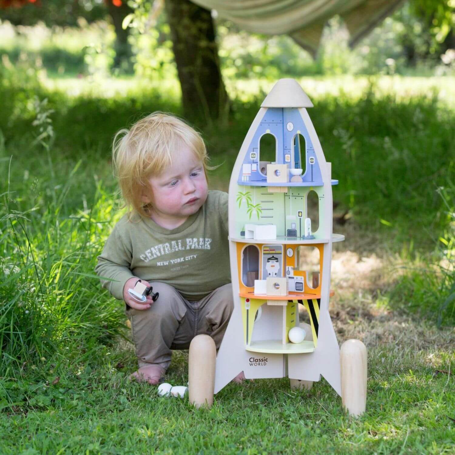 Child exploring the Classic World wooden rocket ship outdoors, featuring intricate details and themed interior rooms for imaginative play.