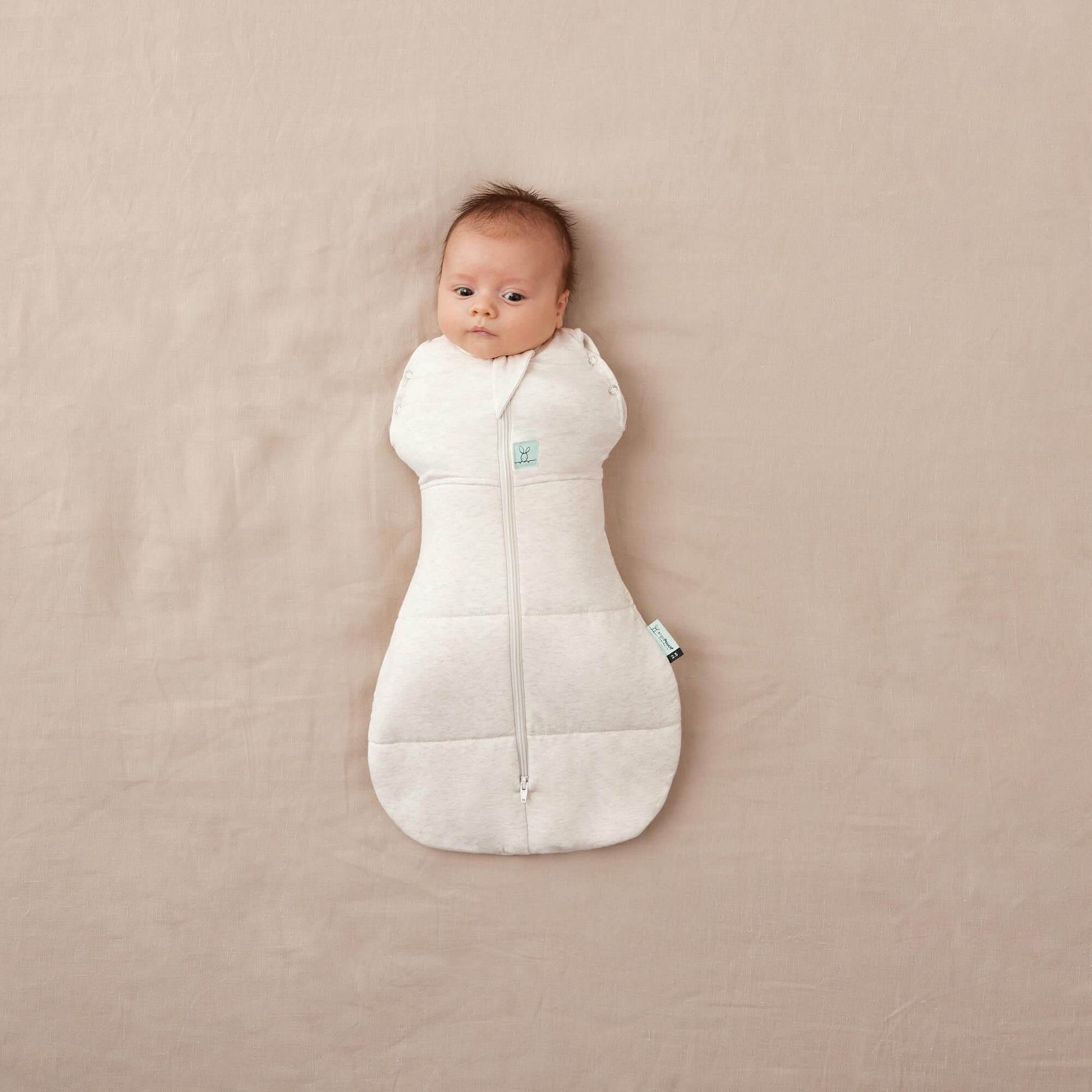 Baby in ErgoPouch Winter 2.5 tog cocoon swaddle bag, oatmeal colour, organic and breathable fabric, perfect for keeping warm in colder weather.