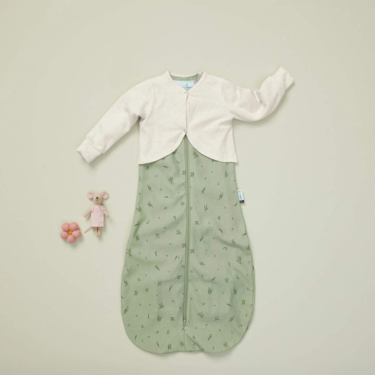 ErgoPouch Long Sleeved Arm Warmer in oatmeal paired with a green sleeping bag, laid flat with a toy mouse and flower. A soft, breathable sleep layer.