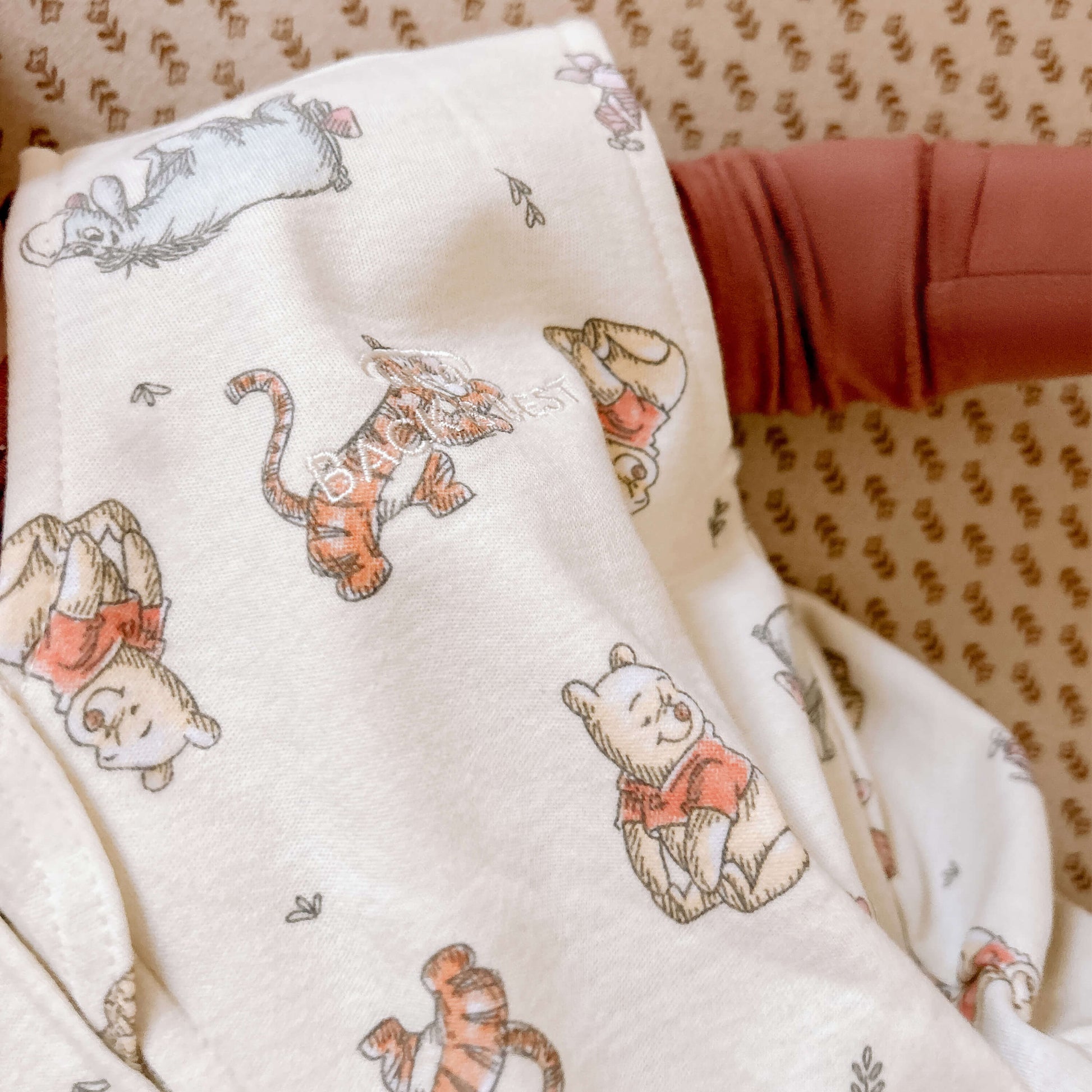 Close-up of HALO® SleepSack® showing quality stitching and "BACK IS BEST" embroidery alongside Winnie the Pooh characters on premium fabric.