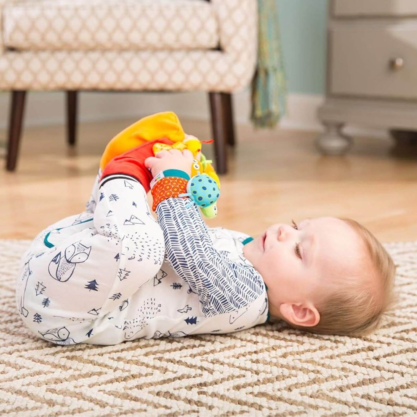 Baby lying on a rug, playing with the Lamaze Gardenbug Foot Finder and Wrist Rattle Set. Colourful bugs encourage sensory exploration.