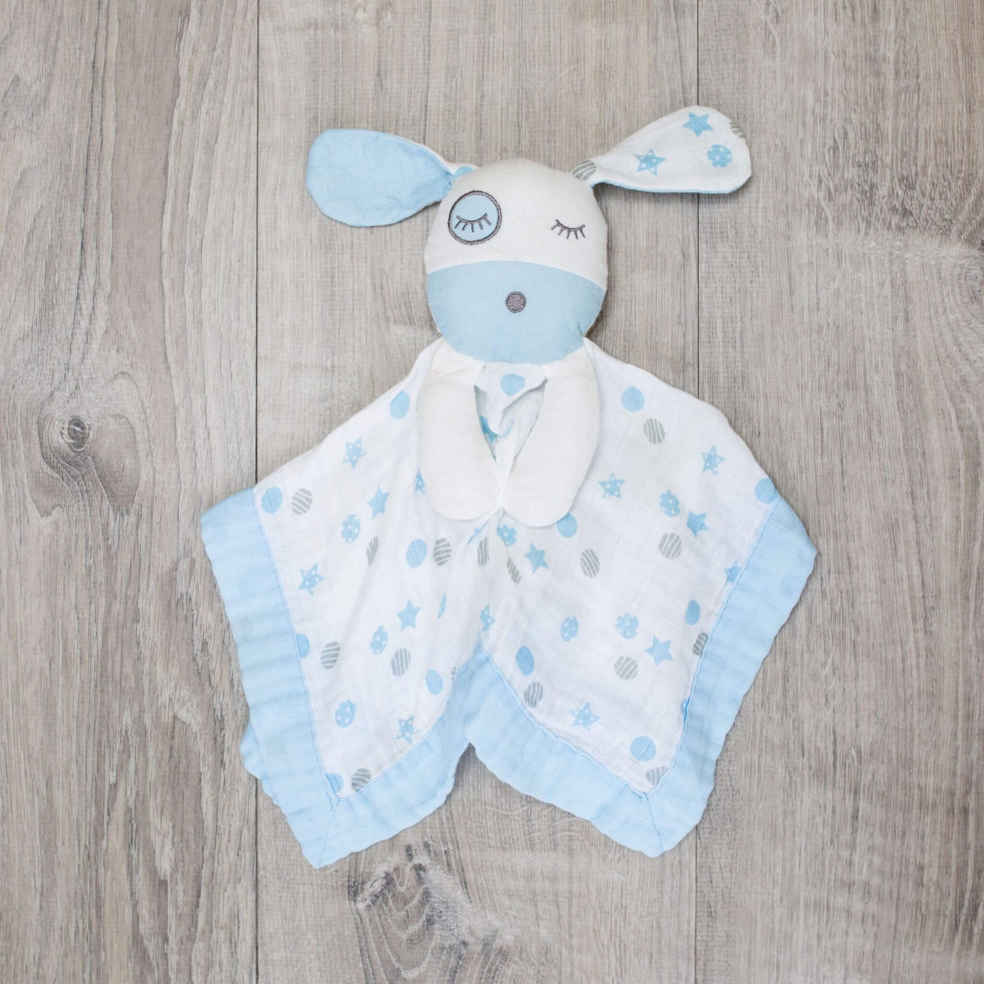  Lulujo Blue Puppy Muslin Lovey displayed on wooden background showcasing the sleeping puppy face design, blue trim and soft muslin fabric.