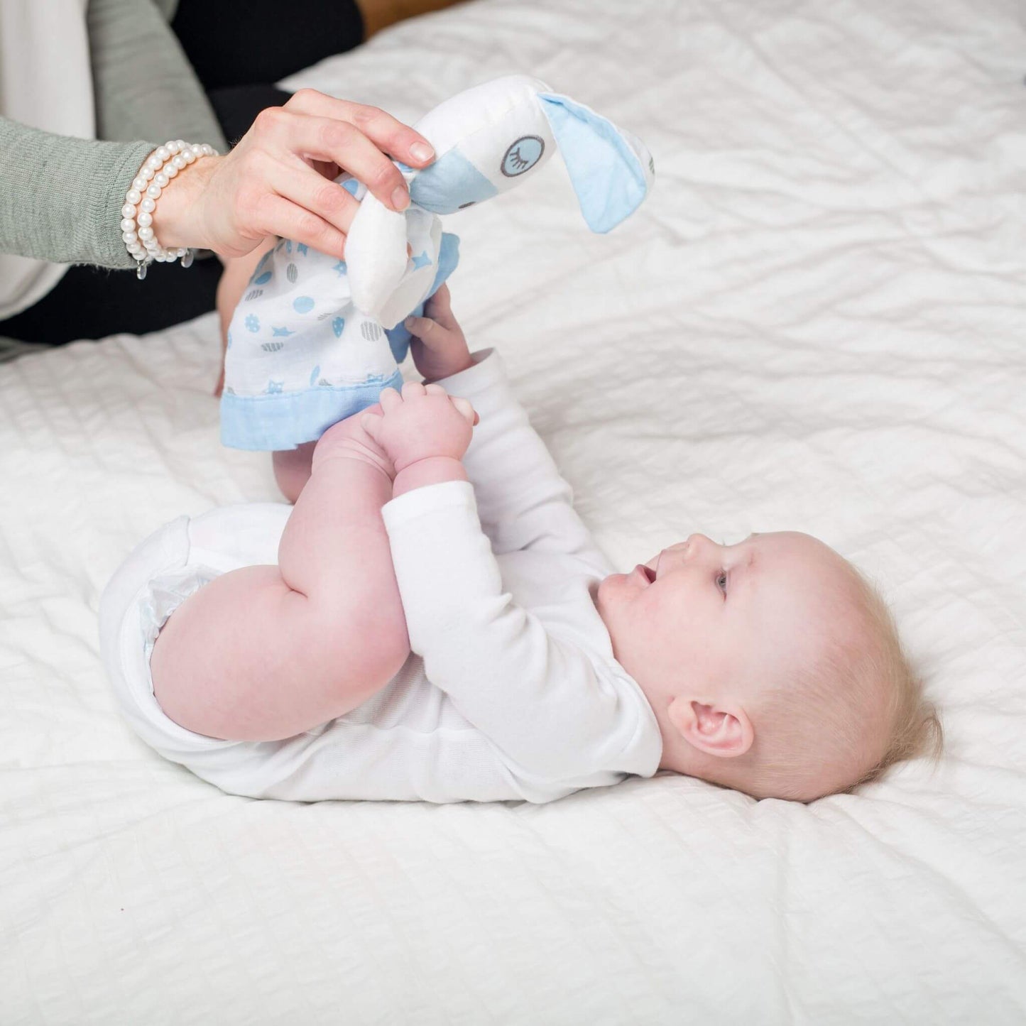 Baby interacting with Lulujo Blue Puppy Muslin Lovey with parent's guidance, demonstrating how the soft security blanket encourages sensory development.