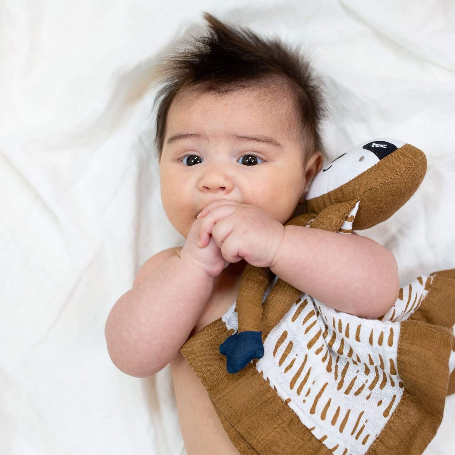 Baby exploring the Lulujo Sloth Muslin Lovey with their mouth, demonstrating how the soft security blanket supports sensory development.