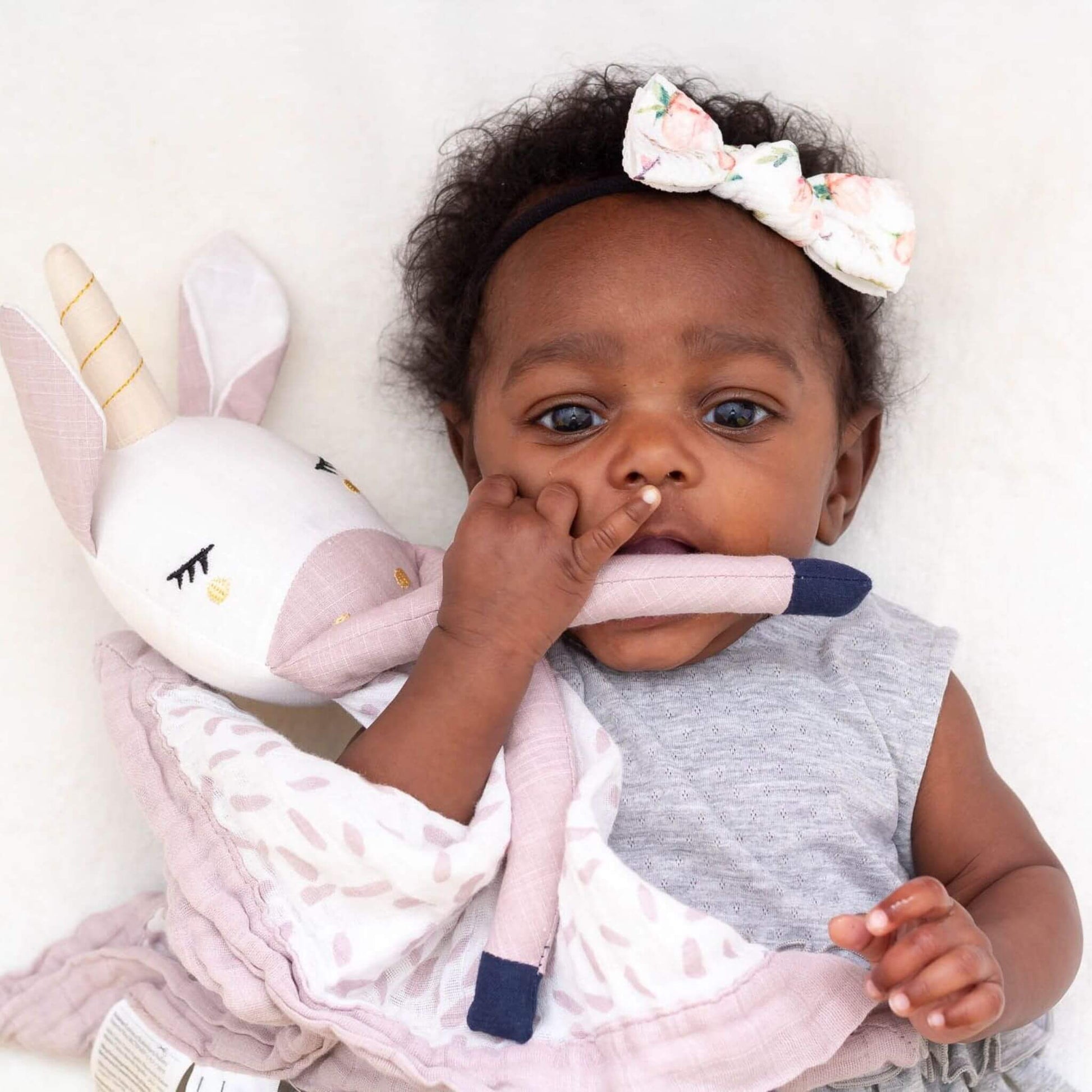 Baby with floral headband exploring the Lulujo Unicorn Muslin Lovey, demonstrating how this comforter encourages tactile development.