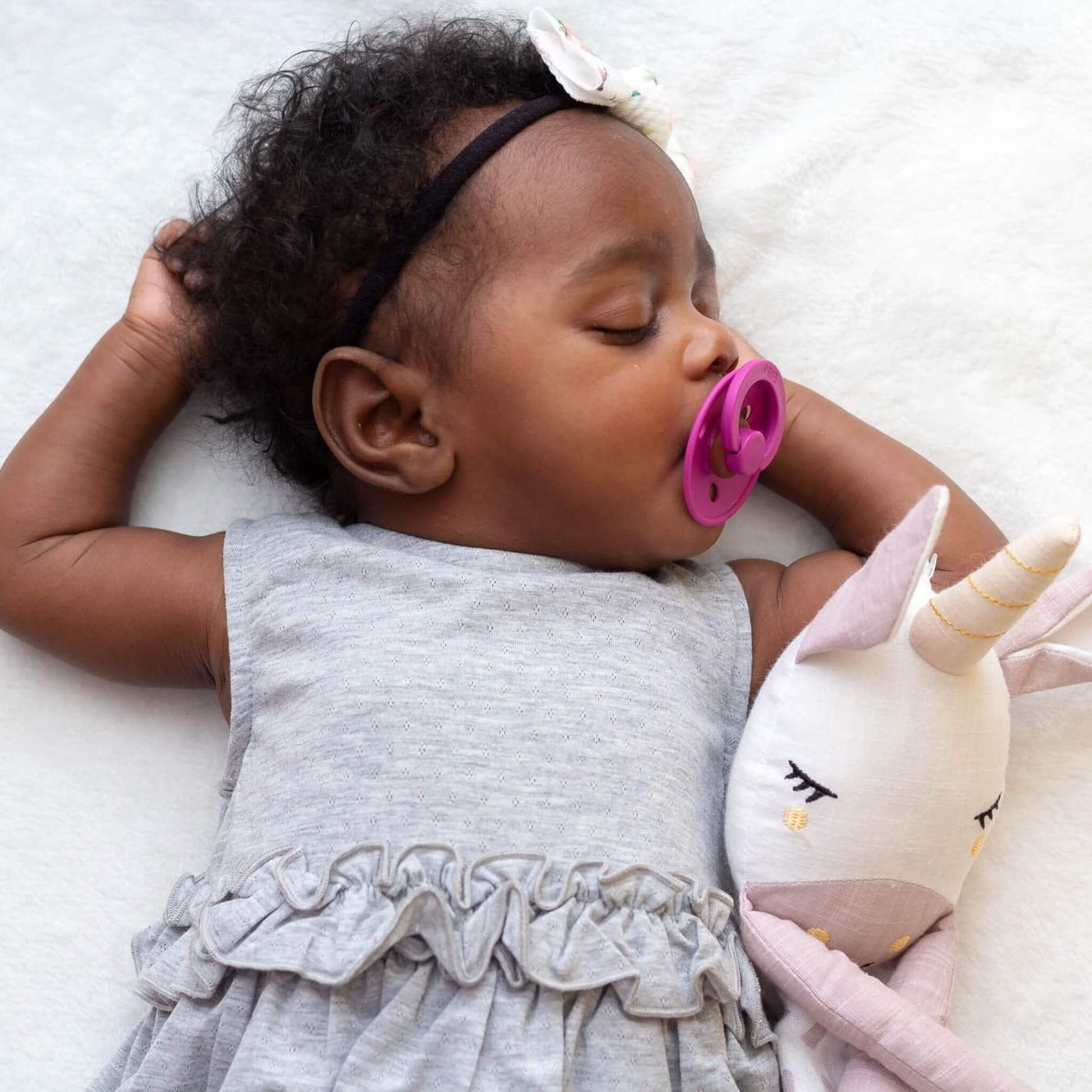 Peaceful sleeping baby with pink pacifier cuddling the Lulujo Unicorn Muslin Lovey, showcasing how it promotes comfort and security during naps.