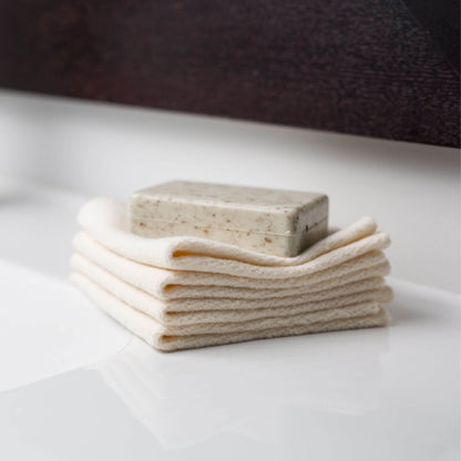 Natural soap bar resting on folded Lulujo Organic Face Cloths, highlighting the eco-friendly bath essentials for sensitive skin.