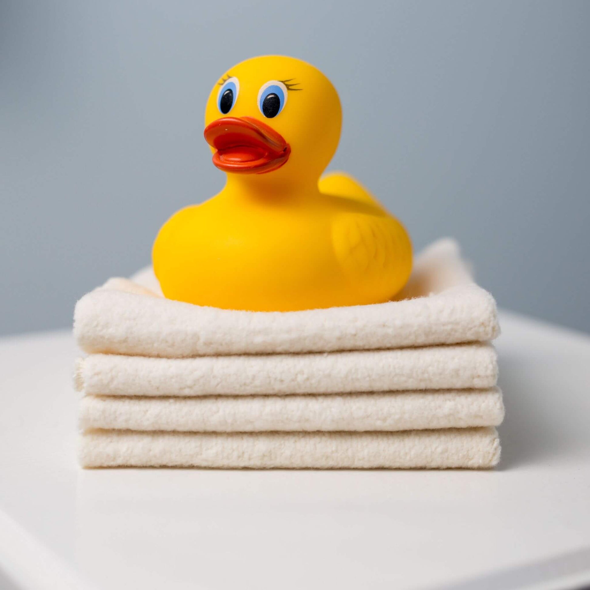 Yellow rubber duck toy placed atop stacked Lulujo Organic Face Cloths, demonstrating the perfect bath time pairing for babies.