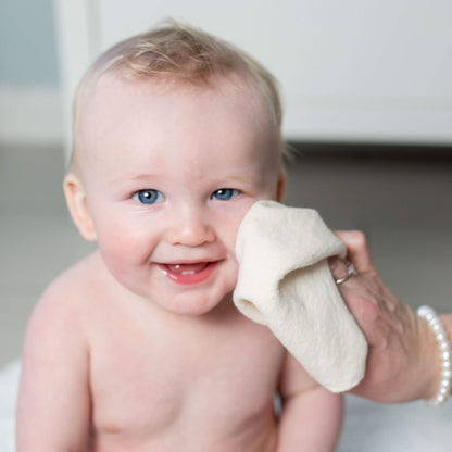 Smiling baby with bright blue eyes having their face gently cleaned with a soft Lulujo Organic Face Cloth during bath time.