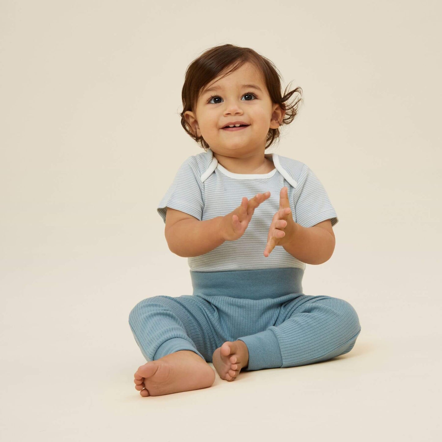 Baby sitting and clapping while wearing a MORI blue Stripe short sleeve bodysuit with white trim, paired with matching blue trousers.